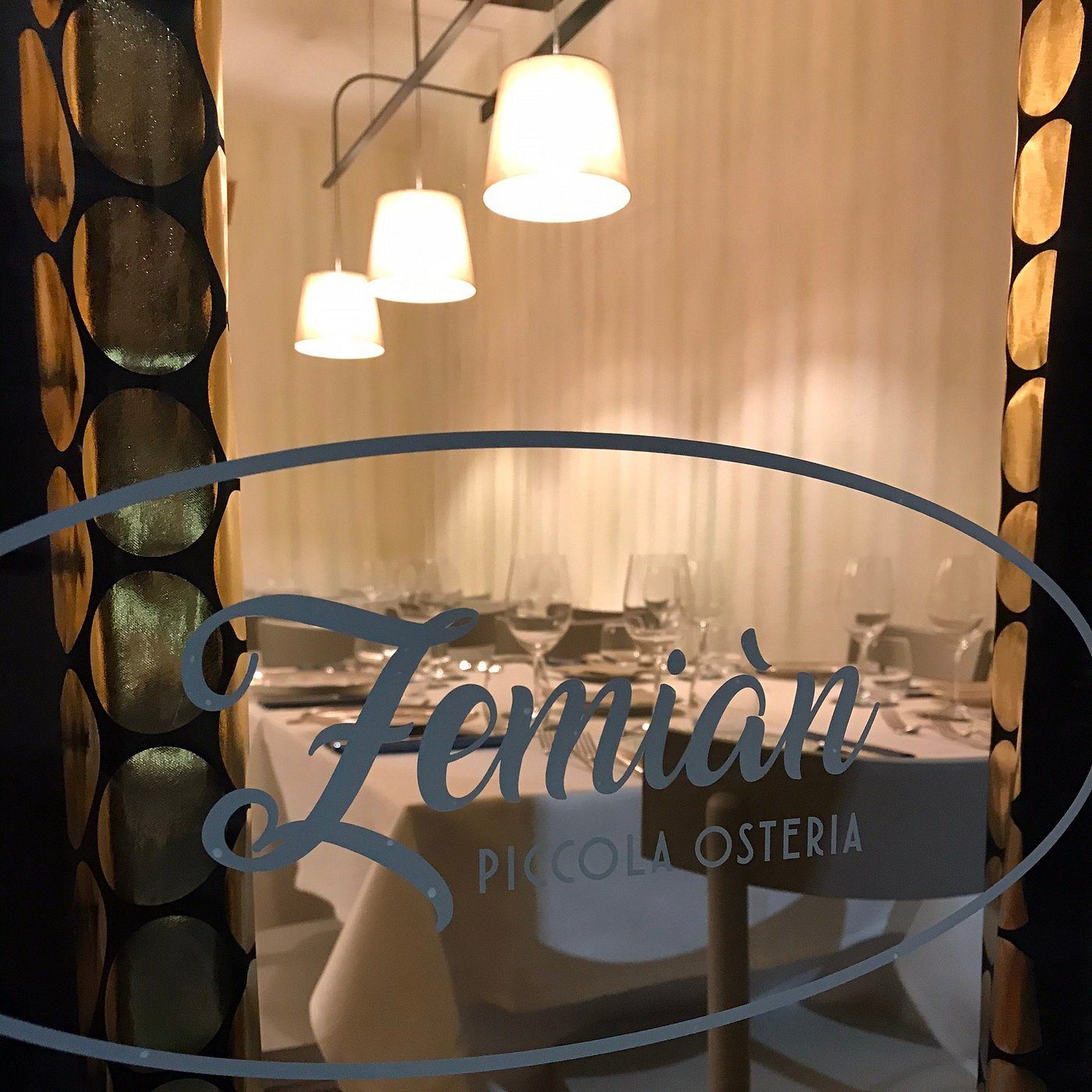 Il logo Zemiàn inciso sulla vetrina, con la sala illuminata dietro